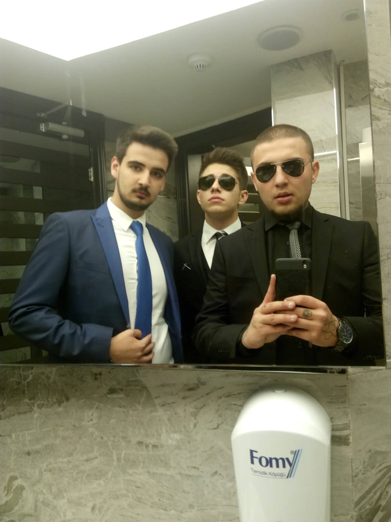 Takım elbiseli üç arkadaşın aynadaki fotoğrafı
